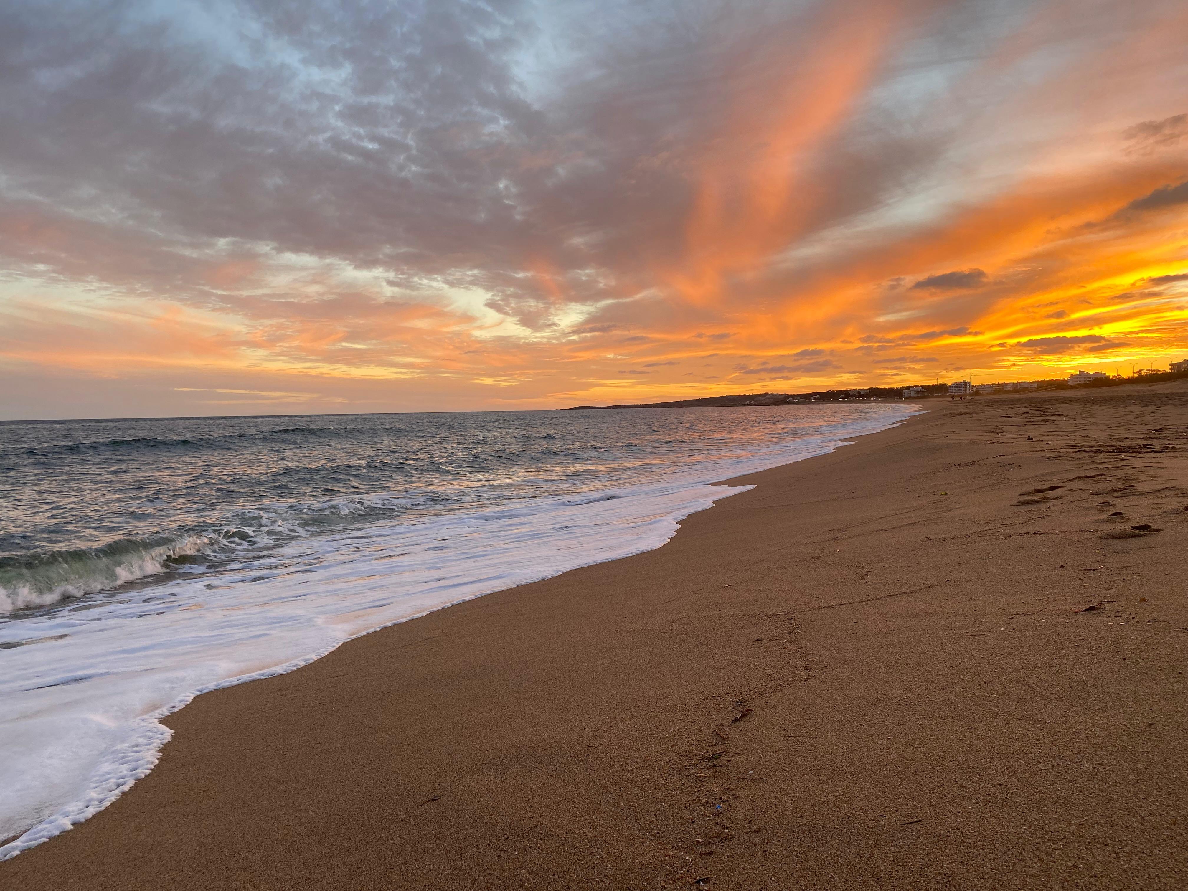 Olas sobre la playa bajo un cielo naranja y rosado al atardecer